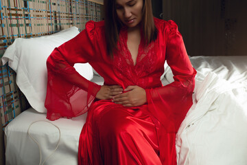 Irritable Bowel Syndrome or IBS. Asian woman in a silk nightgown and red robe suffering from period...