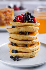 Pancakes with fresh berries and honey on white table. Close-up.