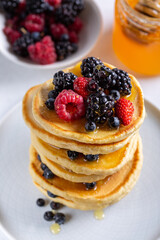 Pancakes with fresh berries and honey on white table. Close-up.
