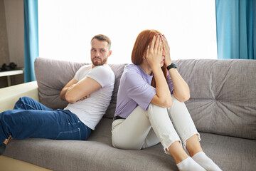 young caucasian couple offended on each other, sit turning away from each other, redhead female and bearded male have quarrel, don't talk