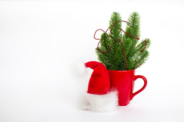 Minimalistic Christmas composition with red mug, Christmas tree decorations and Santa hat isolated on white background. Copy space. Blank for a greeting card.