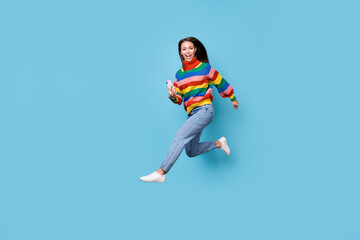 Naklejka na ściany i meble Full length body size profile side view of her she nice attractive cheerful cheery girl wearing casual jumping running using device 5g app fast speed free time isolated blue pastel color background
