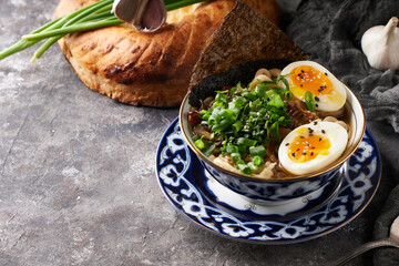 Traditional asian ramen noodle soup with chicken and eggs on gray background