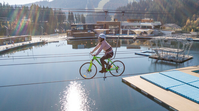 Aerial view of a girl riding a bicycle across a lake on a tightrope