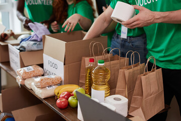 group of diverse people sort through donated food items while volunteering in community, they use...