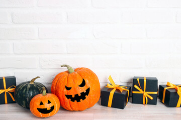 Halloween holiday background with gifts and pumpkin head Jack lantern with funny faces against a white brick wall.