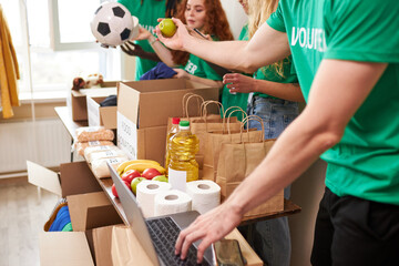 group of diverse people sort through donated food items while volunteering in community, they use...