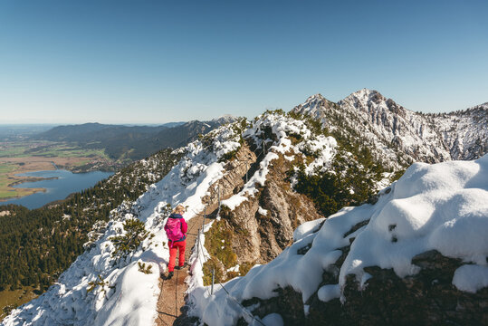 Wanderin im Neuschnee auf dem Gratweg zwischen Heimgarten und Herzogstand mit Blick auf den Kochelsee und Herzogstand-Gipfel