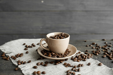 Coffee cup filled of fresh arabica or robusta coffee beans with scattered coffee beans on a linen textile and wood table.