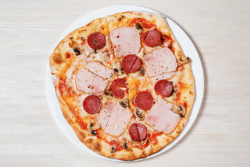 Italian pizza with ham, salami and mushrooms on white plate.