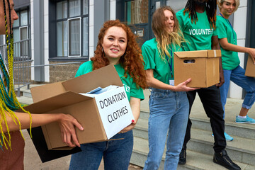 friendly interracial charity group engaged in voluntary, they stand outdoors on stairs transfering...