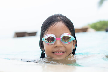 smiling cute little beautiful girl swims with goggles in outdoor swimming pool.