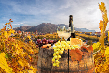 Bottle of white wine with glasses against Weissenkirchen village with autumn vineyards in Wachau...