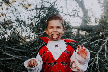 Kid smiling with a dracula halloween costume with a scary wooden background