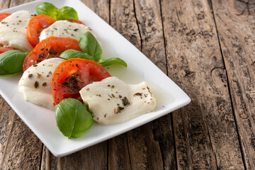 Traditional caprese salad with tomato and mozzarella cheese on rustic wooden table.	Copy space