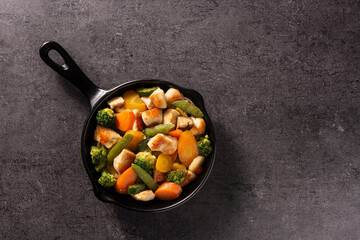 Stir fry chicken with vegetables on iron pan on black background. 	Top view. Copy space