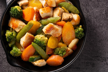 Stir fry chicken with vegetables on iron pan on black background. 	