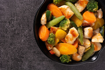 Stir fry chicken with vegetables on iron pan on black background. 	Top view. Copy space