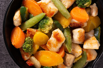 Stir fry chicken with vegetables on iron pan on black background. 	Close up