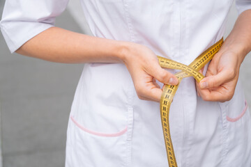 Close up of female hands measure waist volume with centimeter tape. Slim muscular model in a tracksuit