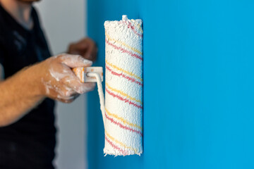 Shot of a man painting the blue wall with a paint roller. Painter painting the walls with a painters roller  at home. Young man painting wall in his apartment. Copy space.