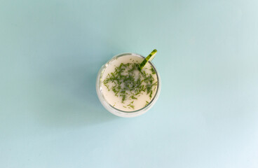 Ayran in a glass glass with dill and a slice of cucumber on a blue background. Fermented product concept. Copy space. Top view.