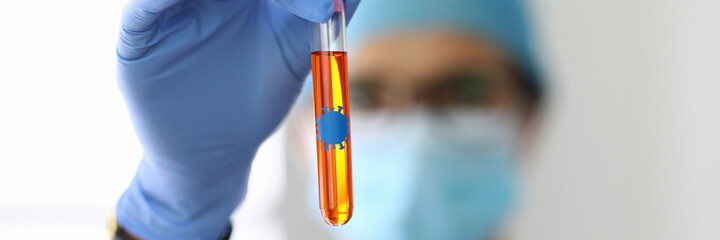 Laboratory assistant in protective mask holds flask with liquid containing bacteria. Investigation of biological material with coronavirus concept