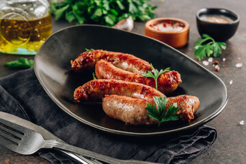 Grilled sausage with greens on black plate over dark background.