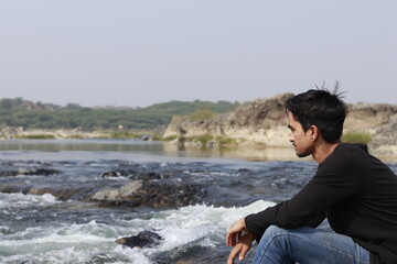 Young indian man sitting on the edge of river site