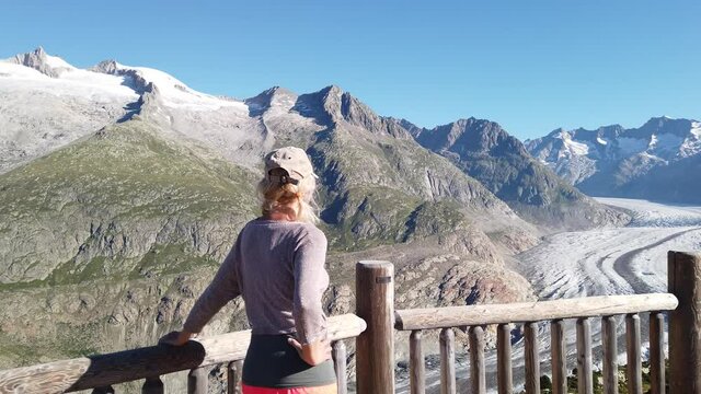 woman looking at Alpine Glacier from Moosfluh viewpoint, Valais Canton, Switzerland, Europe. Sitting tourist woman looking the Alpine glacier. Outdoor activities. Trekking in Swiss Alps in summer