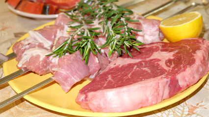 raw kebab and rib eye steak with lemon and rosemary are on a yellow plate.