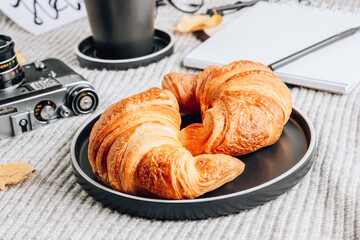Fresh croissant and cup of coffee on a gray knitted background. Cozy autumn morning breakfast composition