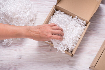 Woman hand putting shredded paper filler to cardboard box