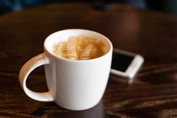 Coffee mug and mobile phone on the table closeup