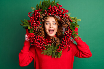 Photo of charming funny girl hold mistletoe wreath look open mouth wear red pullover x-mas headwear isolated green color background