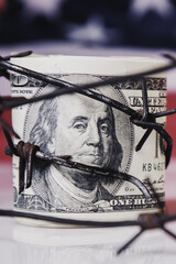 Close up US Dollar bill and barbed wire as symbol of economic warfare, sanctions and embargo busting. Vertical image. - obrazy, fototapety, plakaty