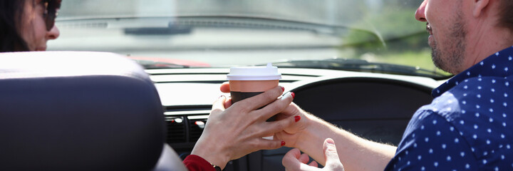 Man and a woman sit in car and hold glass of drink together. Positive communication and meeting concept