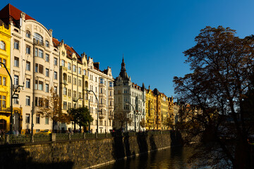 Obraz premium Picturesque view of Prague embankment on bank of Vltava river with peculiar architecture on autumn day, Czech Republic