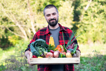 Farmer holding wooden Box full of Vegetables on the organic farm. Portrait of smiling caucasian bearded man in the green garden.