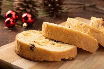 Panettone cut horizontally on a polished wood, pine cones and Christmas balls on rustic wood, black background, selective focus.