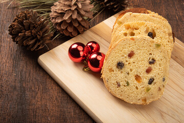 Panettone cut horizontally on a polished wood, pine cones and Christmas balls on rustic wood, black background, selective focus.