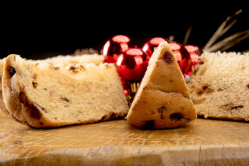 Arrangement with slices of panettone, pine cones and Christmas balls on rustic wood, black background, selective focus.