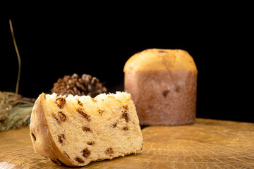 Arrangement with panettone and panettone slices, pine cones on rustic wood, black background, selective focus.