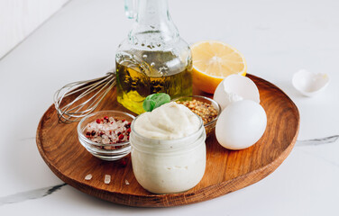 Homemade mayonnaise sauce with ingredient - olive oil, eggs, mustard and lemon on a wooden plate.