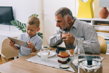 grandfather and grandson using tablet while having breakfast at home
