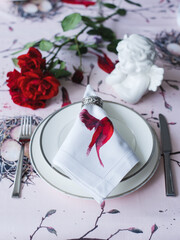 Table setting with a rose. Napkin with a bird and an angel on a bright tablecloth