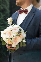 Elegant man in a three-piece suit with a burgundy bow tie holds a round bouquet with eustoma and roses