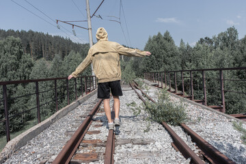 a man walks across an abandoned railway bridge. old iron bridge in the forest across the road.