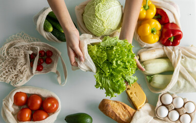 Woman's hand, holding a reusable grocery bag with vegetables on a kitchen at home and takes salad out. Zero waste and plastic free concept. Mesh cotton shopper with vegetables. Ecology.