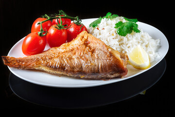 Sea bass grill with rice, greenery and cherry tomatoes. Black background.
